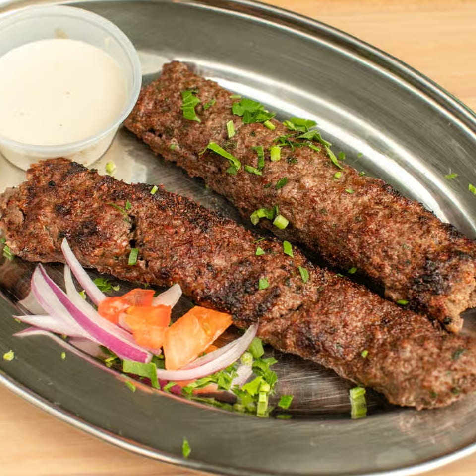 Two grilled Lebanese Shwarmas kofta kebabs with chopped onions, tomatoes, and a side of sauce.
