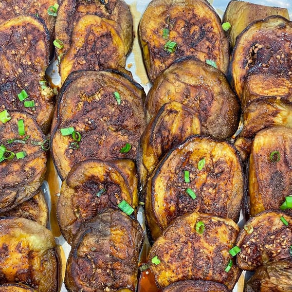 Close-up of many slices of roasted eggplant, garnished with green onions and sesame seeds.