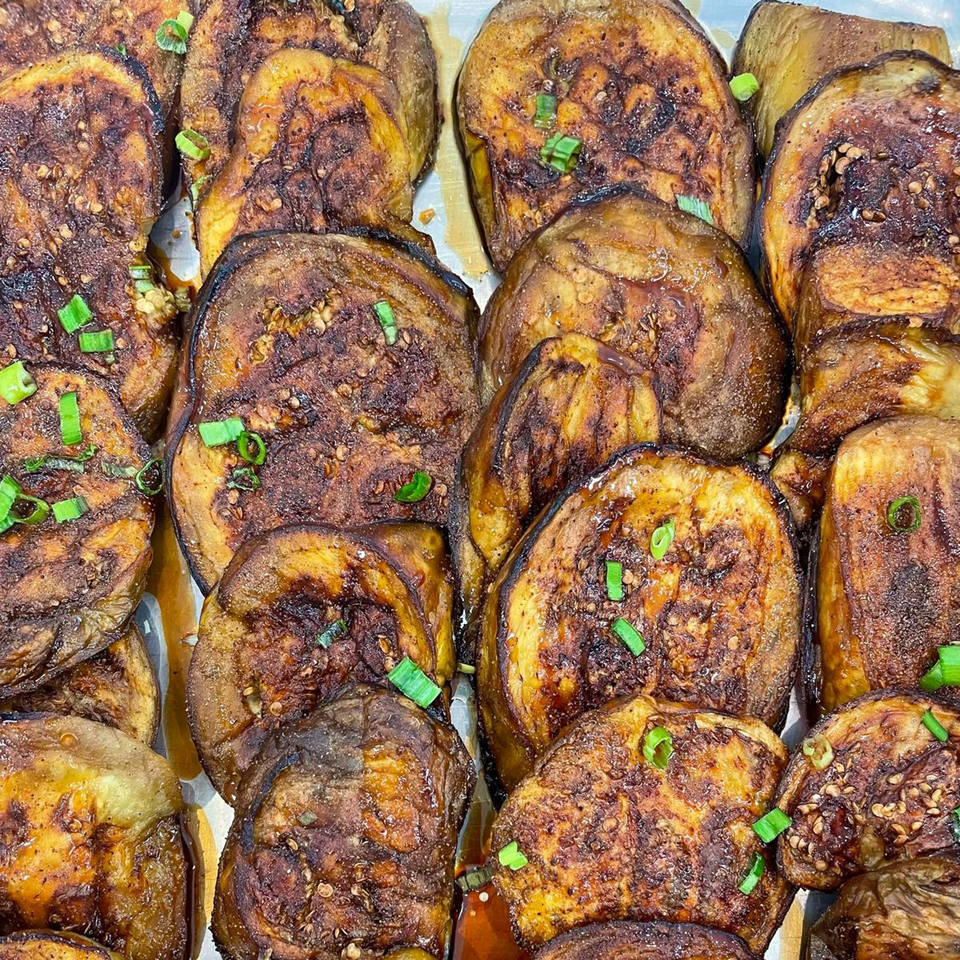 Close-up of many slices of roasted eggplant, garnished with green onions and sesame seeds.