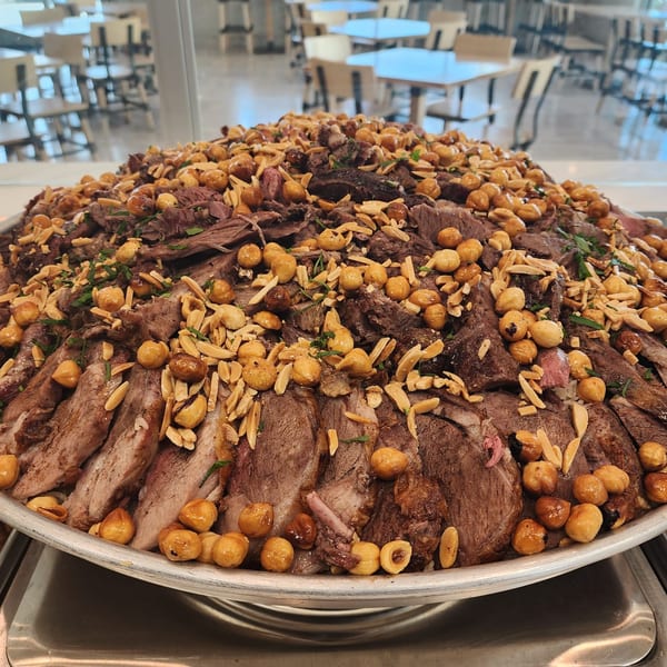 A large platter of sliced Lebanese meat, topped with chickpeas, almonds, and herbs.