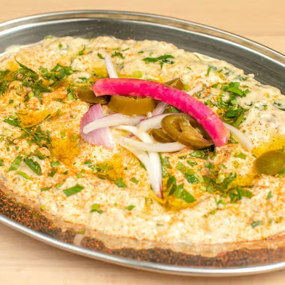 Creamy Lebanese hummus topped with parsley, red onions, jalapeños, and a pink pickled turnip.