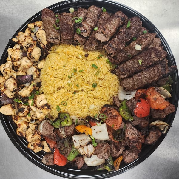A large platter of Lebanese food with yellow rice, chicken, beef kebabs, and grilled vegetables.