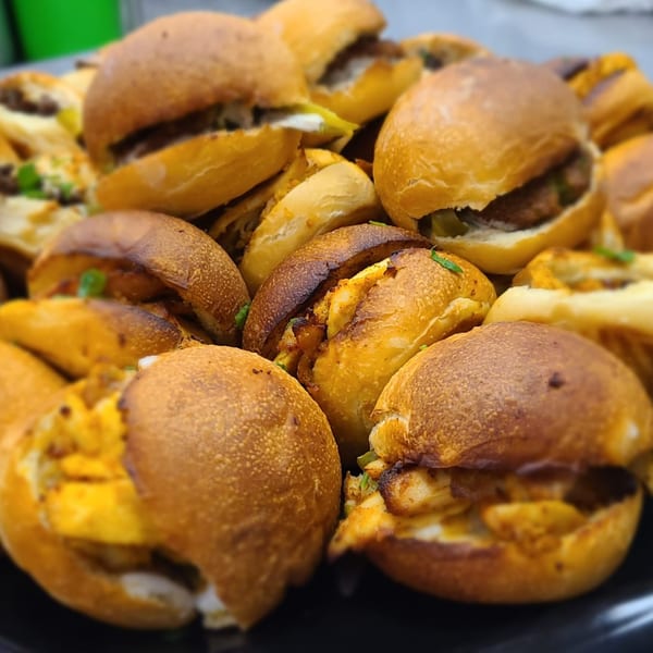 A close-up of numerous mini Lebanese shawarma sandwiches with golden buns on a black platter.