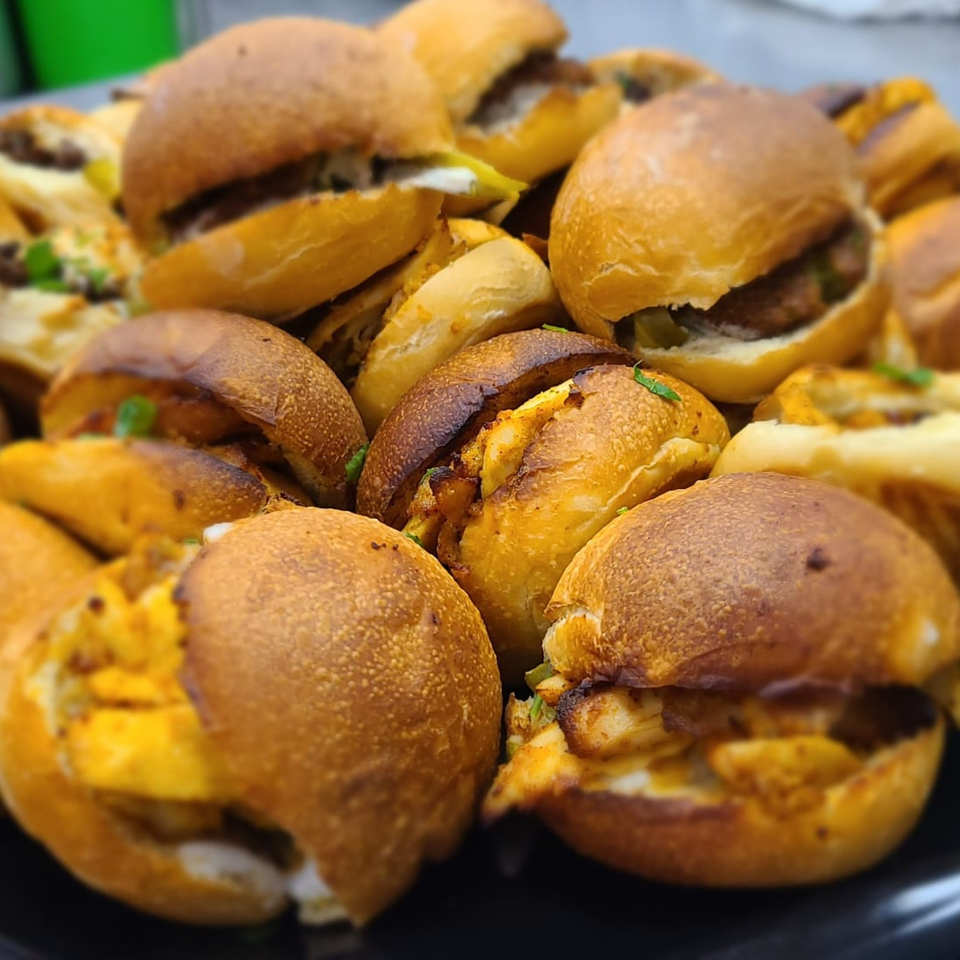 A close-up of numerous mini Lebanese shawarma sandwiches with golden buns on a black platter.
