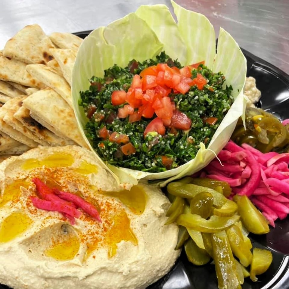 A Lebanese platter with hummus, pita bread, tabbouleh, pickled turnips, and cucumbers.