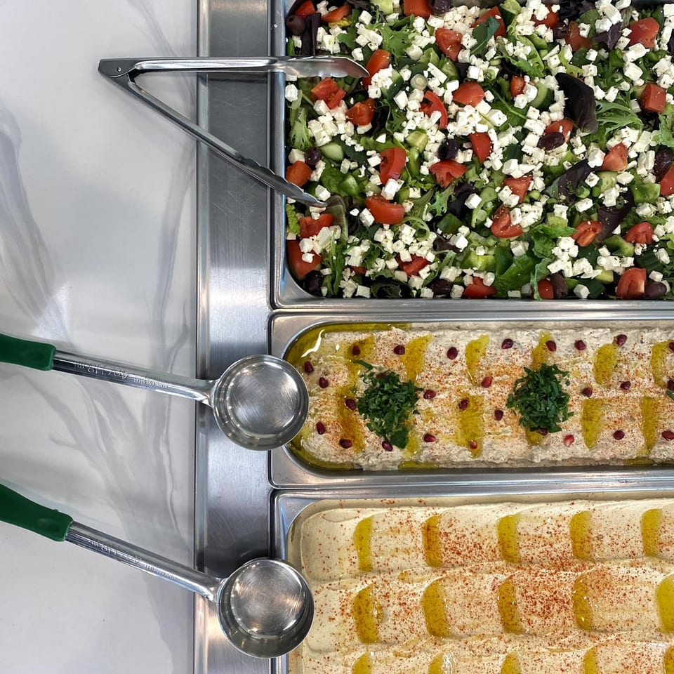 Top-down view of three Lebanese dishes: salad, baba ghanoush, and hummus, in a buffet line.