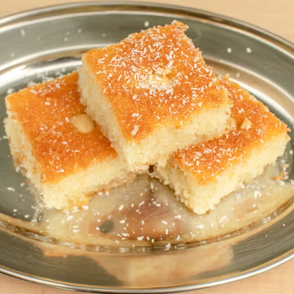 Three pieces of Lebanese semolina cake (Basbousa) with coconut flakes on a silver platter.
