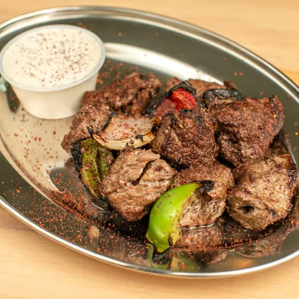 Lebanese grilled meat skewers with onions, peppers, and a side of white sauce on a metal tray.