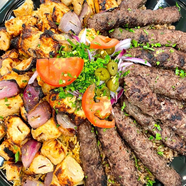 A platter of Lebanese Shish Tawook and Kofta kebabs with rice, garnished with tomatoes, onions, and jalapeños.