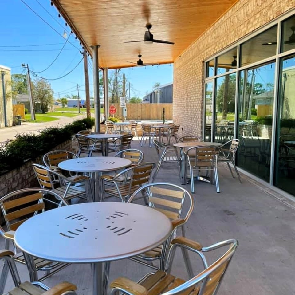 Outdoor patio of Shwarmas with several round tables and chairs under a wooden ceiling with fans.
