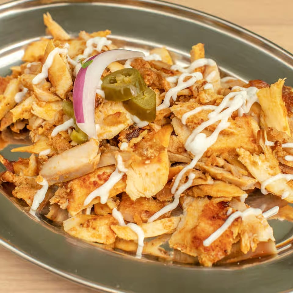 Shredded Lebanese chicken shawarma with white sauce, red onion, and jalapeños on a metal plate.